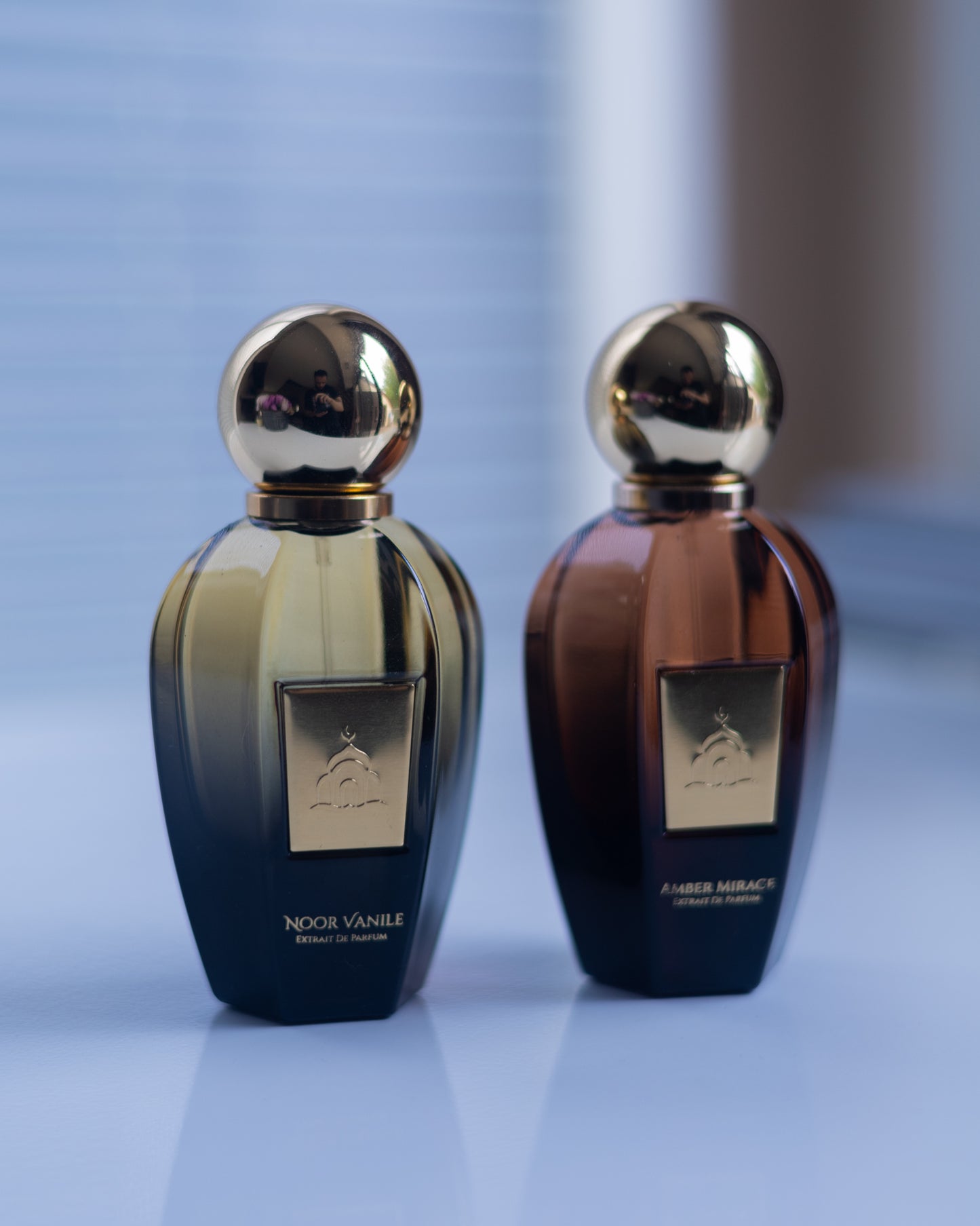 Two perfume bottles with gold caps on a reflective surface