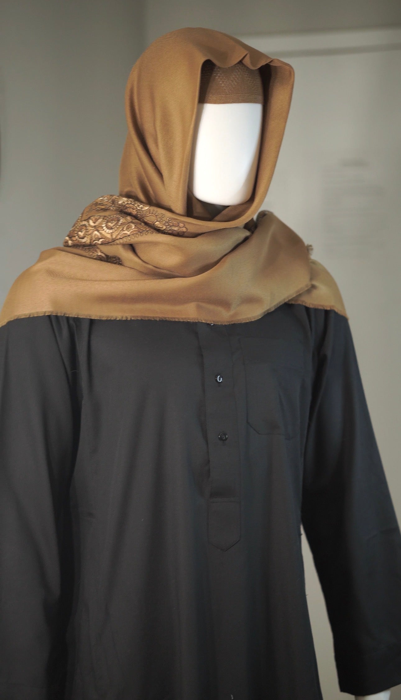 Mannequin wearing a brown shemagh and black garment against a plain background