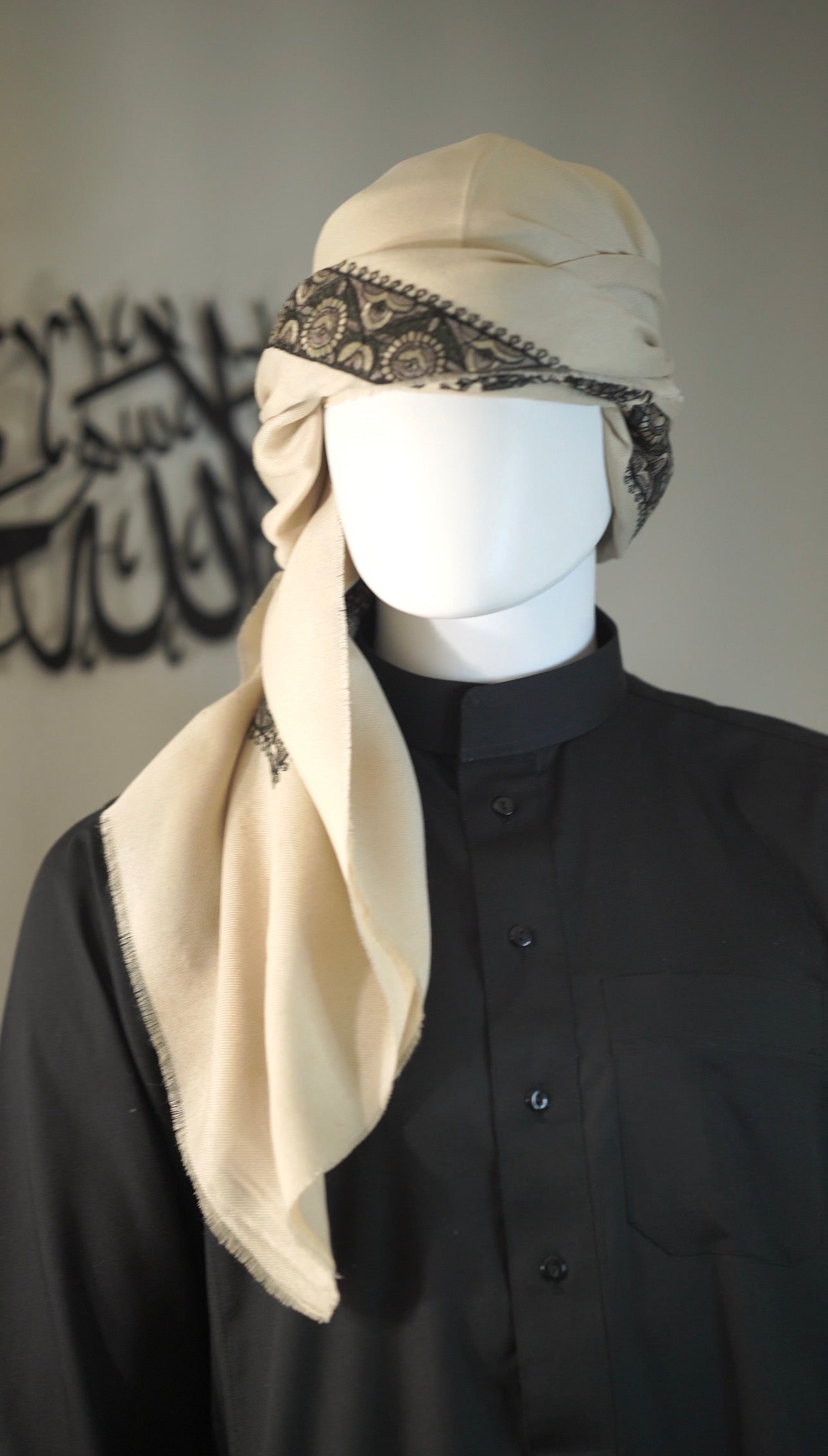 Mannequin wearing a black outfit with a beige shemagh and decorative bandana against a neutral background.