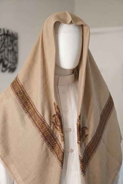 A beige shemagh with brown embroidered borders and motifs, draped over a white button-up shirt on a white mannequin torso.