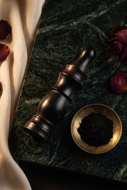 Ebony wood kohl applicator on dark marble beside a brass dish of kohl powder
