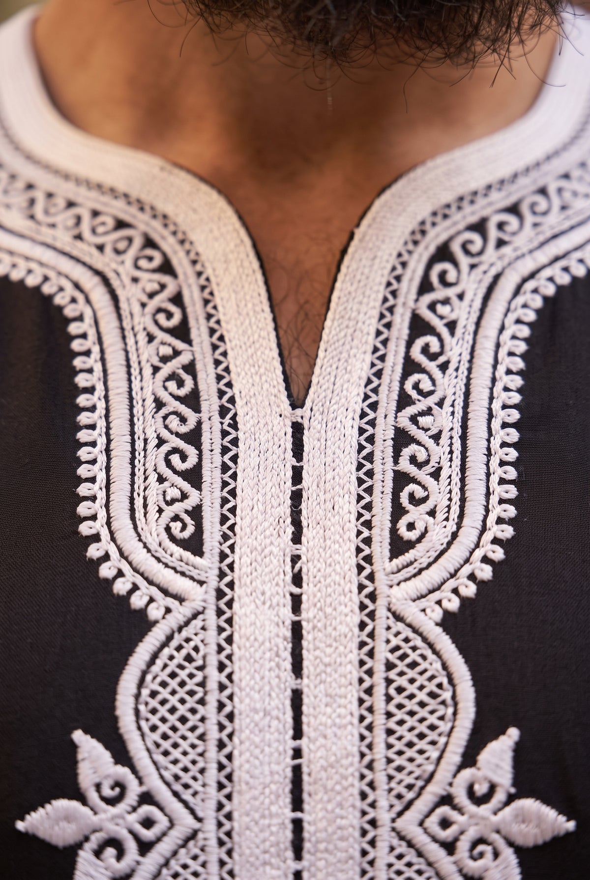 Close-up of a black Morrocan thobe with intricate white embroidery around the V-neck and upper chest, worn by a person.