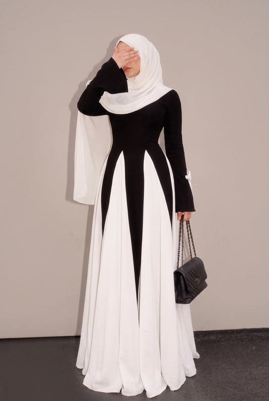 Woman wearing a black and white color block abaya maxi dress with white hijab, front view