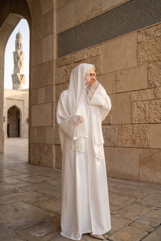 Bride wearing a white katb ktab bridal open abaya set with lace cuffs and matching veil in a mosque courtyard