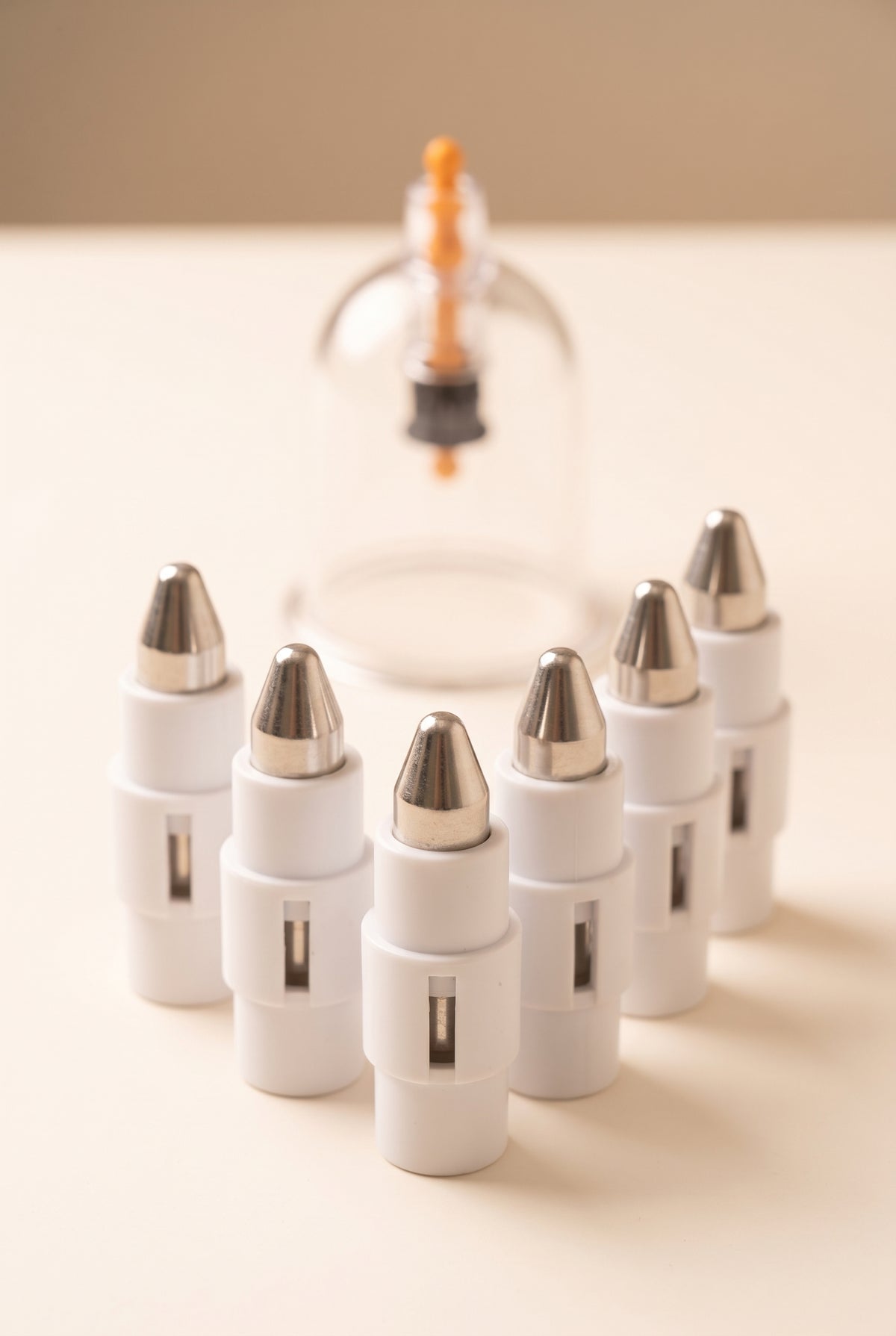 Six pressure point attachments with blunt metal tips in front of a clear hijama cup