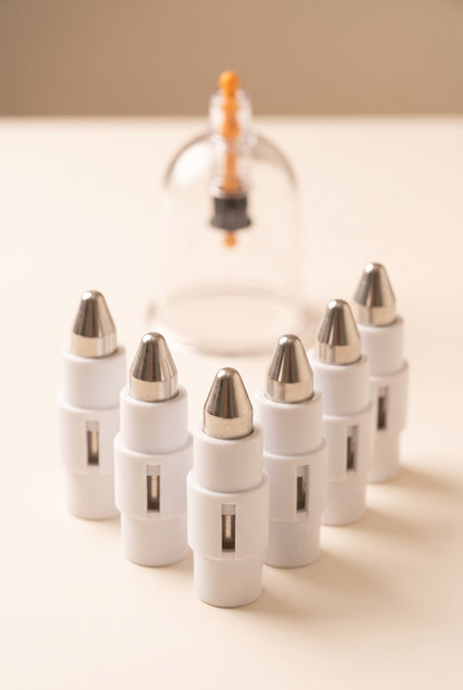 Six pressure point attachments with blunt metal tips in front of a clear hijama cup