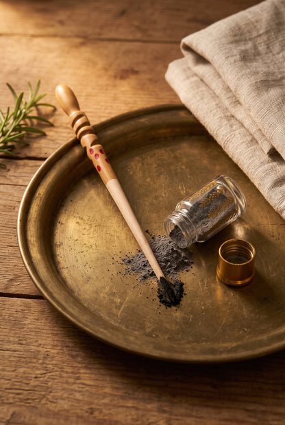 Wooden kohl stick resting on a brass tray beside an open bottle of kohl