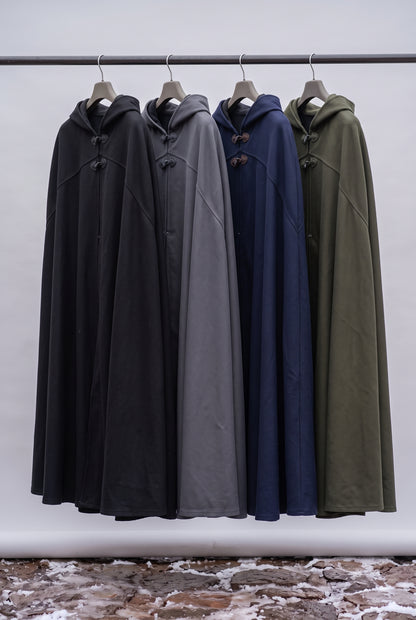 Four hooded cloaks or long coats hanging on a metal rack against a plain light wall. The garments are shown in four colorways: black, charcoal gray, navy blue, and olive green. Arabian Burnous – Hooded Winter Cloak Cape with Toggle Closure | Warm Oversized Djellaba Coat for Men