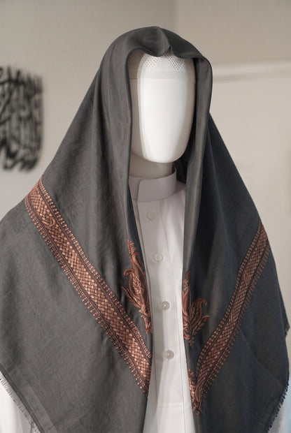 A dark gray shemagh with brown embroidered borders and motifs, draped over a white button-up shirt on a white mannequin torso.