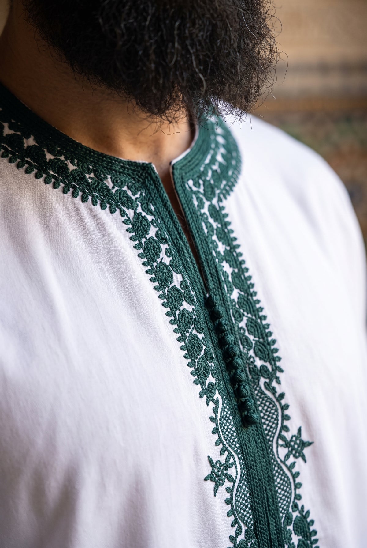 Close-up of a person wearing a white Morrocan thobe with dark green embroidered lace trim around the collar and front placket.