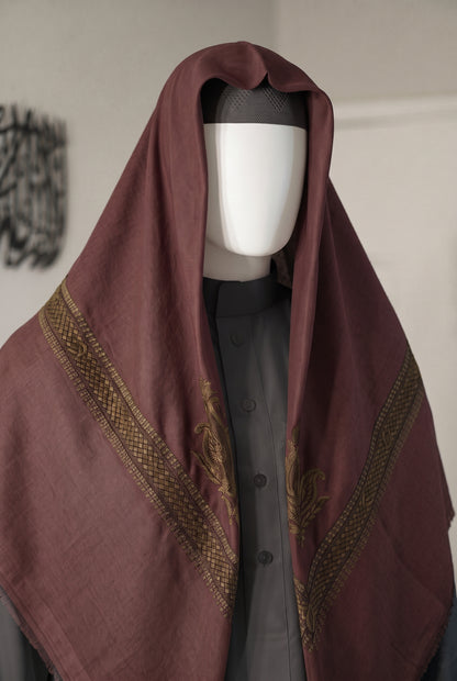 A large draped shemagh in a deep burgundy color with gold patterned borders, displayed on a white mannequin torso over a dark gray button-up thobe.