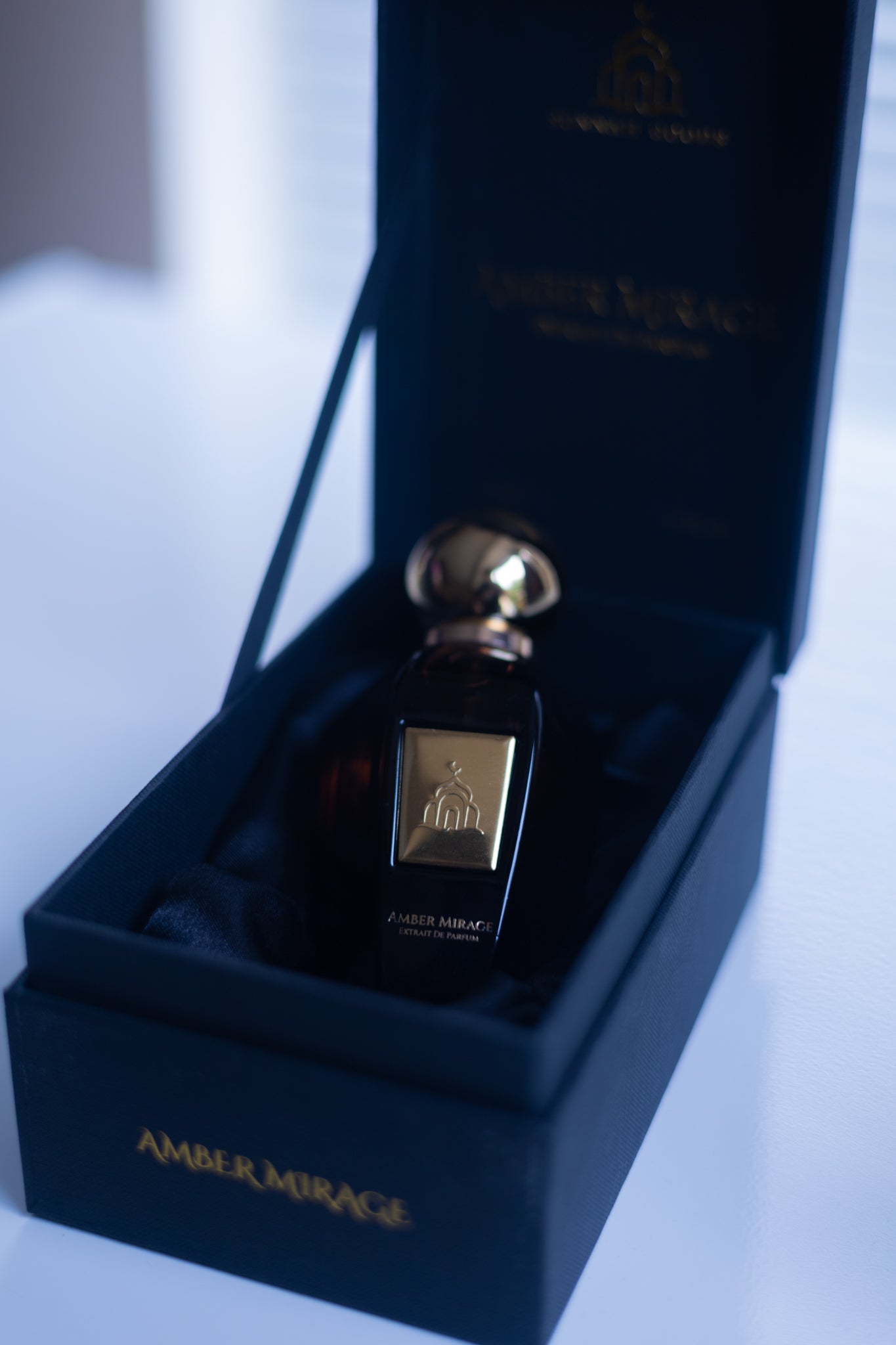 Perfume bottle with gold cap in a dark blue box on a light gray background