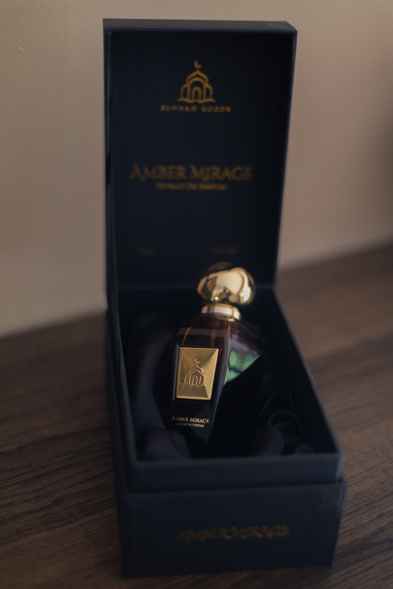 Amber Mirage perfume bottle in a blue box on a wooden surface